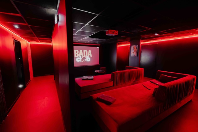 Salle lounge avec écran et canapés rouges au Bada Club